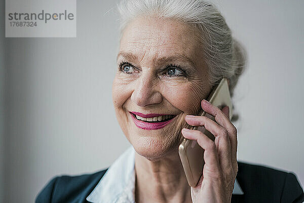 Glückliche ältere Geschäftsfrau  die vor weißem Hintergrund mit dem Mobiltelefon spricht