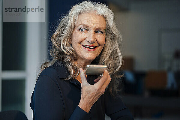 Glückliche ältere Frau  die im Büro Voicemail über ihr Smartphone sendet