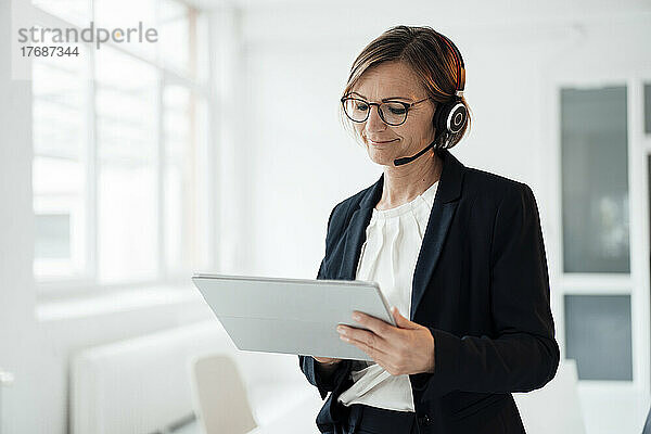 Lächelnder Telefonanrufer mit Headset und Tablet-PC im Büro