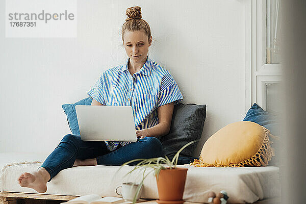 Berufstätige Frau sitzt mit Laptop zu Hause im Bett