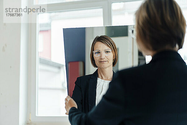 Geschäftsfrau schaut durch Spiegelreflexion im Büro