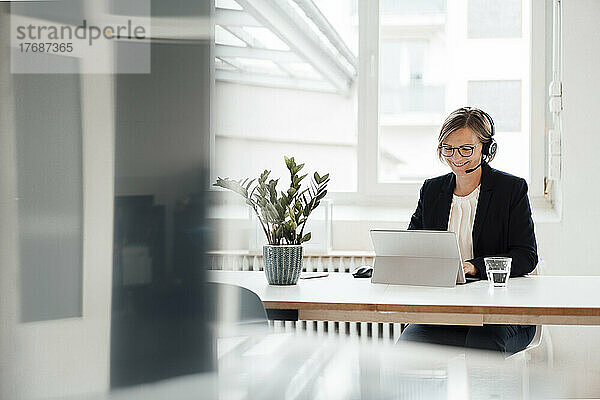 Glückliche Geschäftsfrau mit Headset  die über einen Tablet-PC bei einem Videoanruf spricht