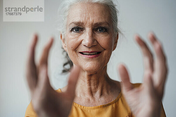 Glückliche ältere Frau gestikuliert vor weißem Hintergrund