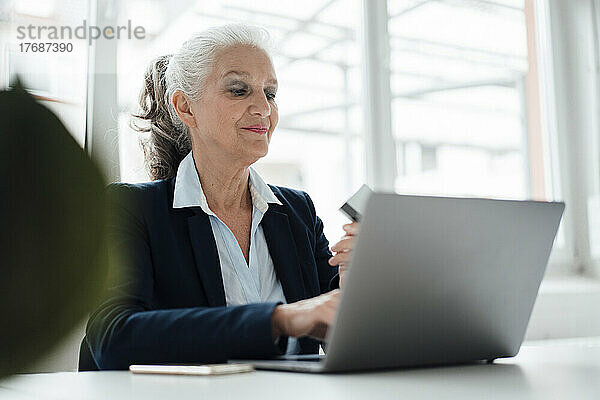 Lächelnde Geschäftsfrau mit Karte  die im Büro am Laptop arbeitet