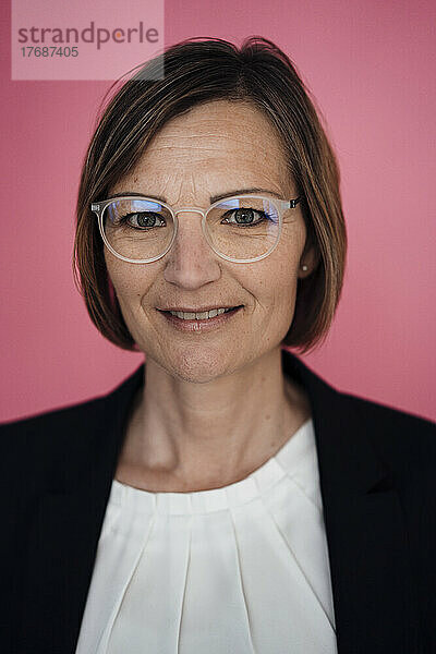 Lächelnde Geschäftsfrau mit Brille vor rosa Hintergrund