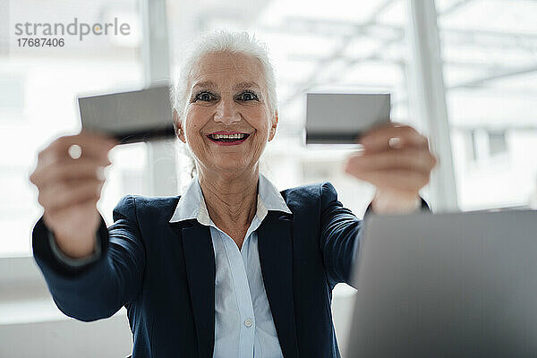 Glückliche ältere Geschäftsfrau  die im Büro Visitenkarten zeigt