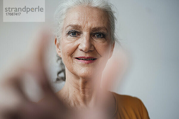 Lächelnde ältere Frau mit grauem Haar gestikuliert vor weißem Hintergrund