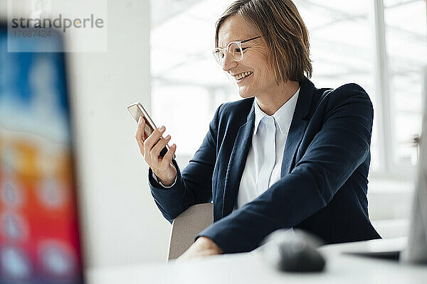 Glückliche Geschäftsfrau  die im Büro ihr Smartphone benutzt