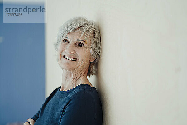 Glückliche ältere Frau mit grauen Haaren lehnt an der Wand