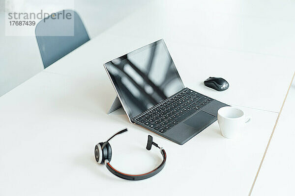 Tablet-PC mit Headset und Kaffeetasse auf weißem Schreibtisch im Büro