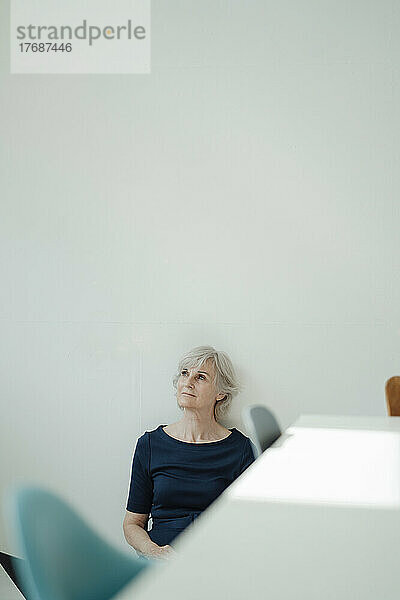 Ältere Geschäftsfrau mit grauen Haaren sitzt vor der Wand