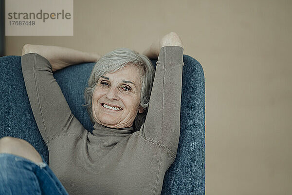 Glückliche ältere Frau sitzt auf einem Stuhl vor der Wand