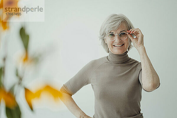 Glückliche ältere Frau mit Brille steht vor der Wand