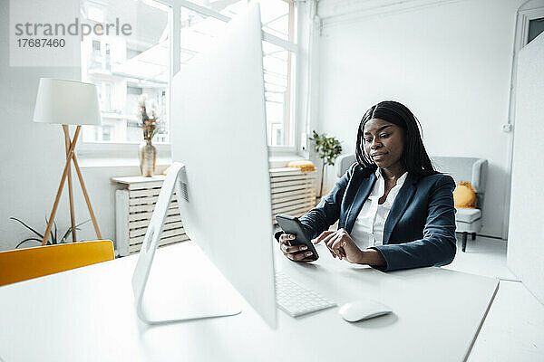 Geschäftsfrau benutzt Smartphone am Schreibtisch im Büro