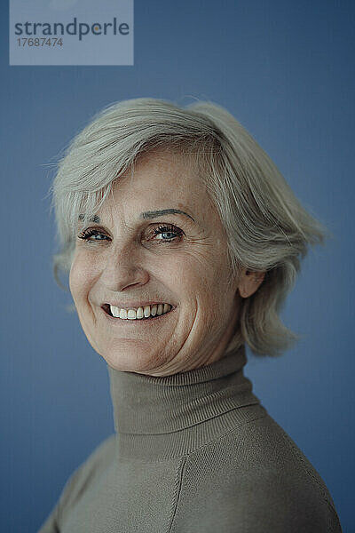 Glückliche ältere Frau mit grauen Haaren vor blauem Hintergrund