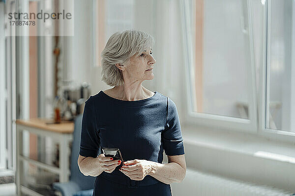 Ältere Geschäftsfrau mit grauem Haar hält Smartphone im Büro
