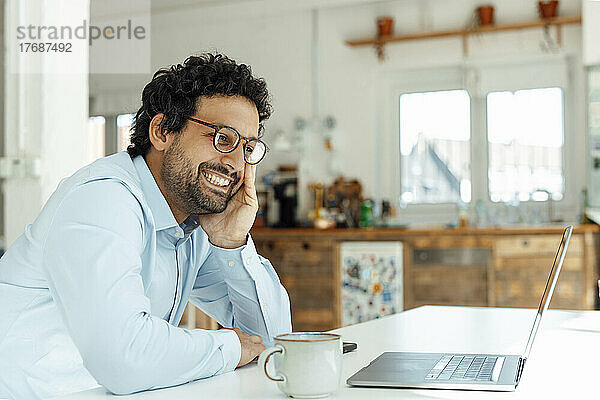 Glücklicher Geschäftsmann mit Brille und Blick auf Laptop im Büro