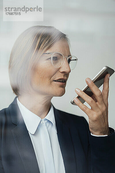 Geschäftsfrau mit braunem Haar spricht über den Lautsprecher ihres Mobiltelefons