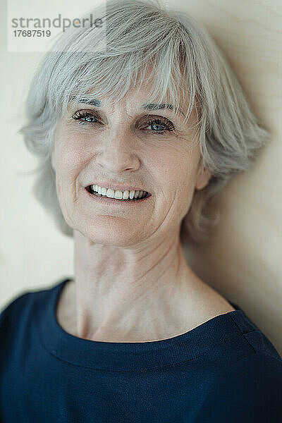 Lächelnde ältere Frau mit grauen Haaren vor der Wand
