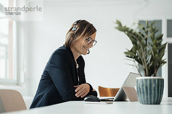 Lächelnde Geschäftsfrau mit Headset  die über einen Tablet-PC bei einem Videoanruf spricht
