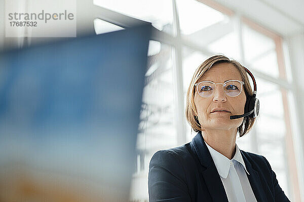 Lächelnder Telefonanrufer mit Headset sitzt im Büro