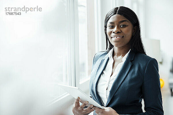Lächelnde Geschäftsfrau mit Tablet-PC am Fenster im Büro