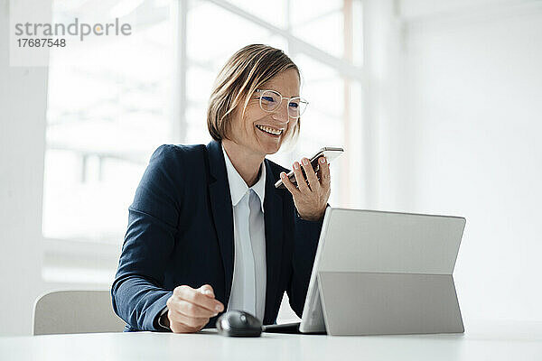 Glückliche Geschäftsfrau  die am Schreibtisch im Büro sitzt und mit dem Mobiltelefon spricht