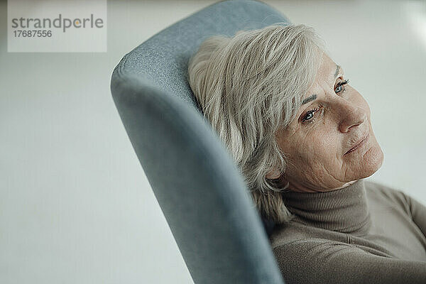 Nachdenkliche ältere Frau mit grauen Haaren sitzt auf einem Stuhl