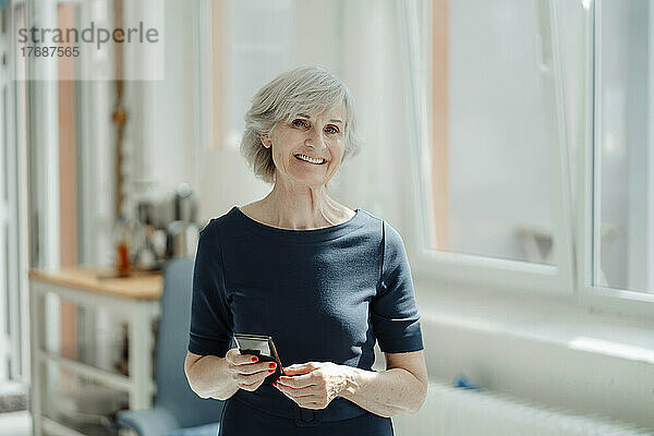 Lächelnde ältere Geschäftsfrau mit Mobiltelefon im Büro