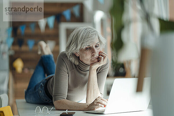 Ältere Frau mit Kopf in der Hand und Laptop  der auf dem Schreibtisch im Büro liegt