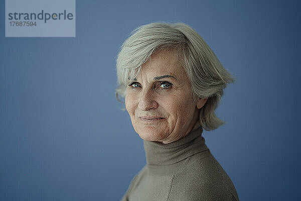 Lächelnde ältere Frau mit grauen Haaren vor blauem Hintergrund