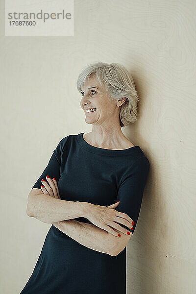 Smiling senior woman with arms crossed leaning on wall