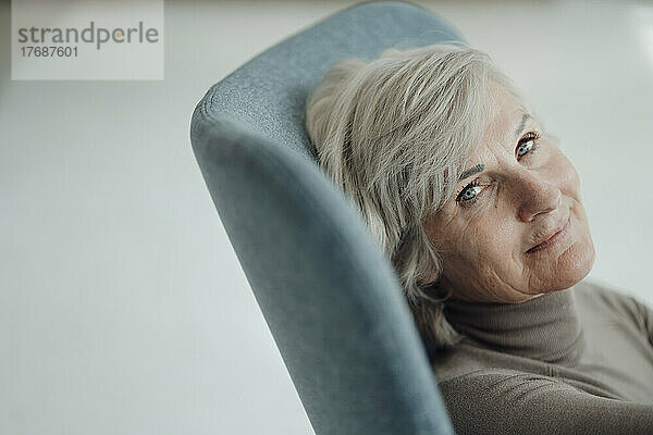 Lächelnde ältere Frau mit grauen Haaren sitzt auf einem Stuhl