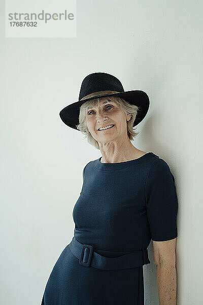 Smiling senior woman wearing hat standing against white background