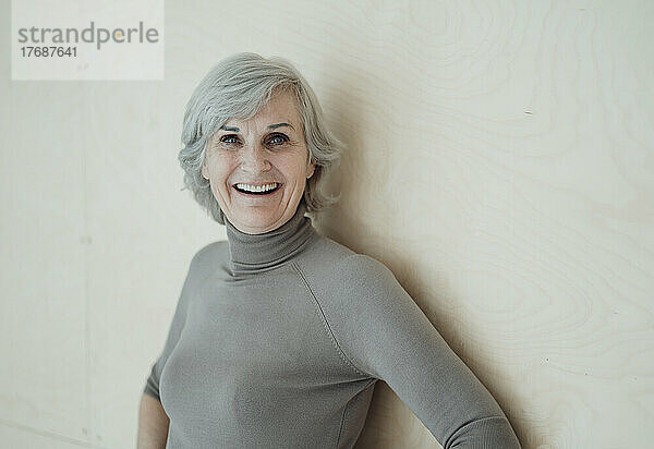 Happy senior woman with gray hair standing in front of wall
