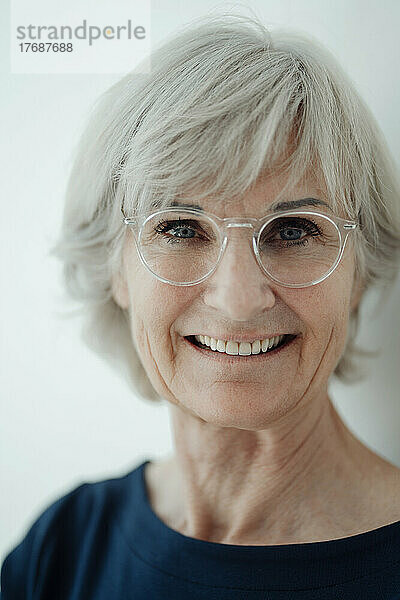 Lächelnde ältere Frau mit Brille vor weißem Hintergrund
