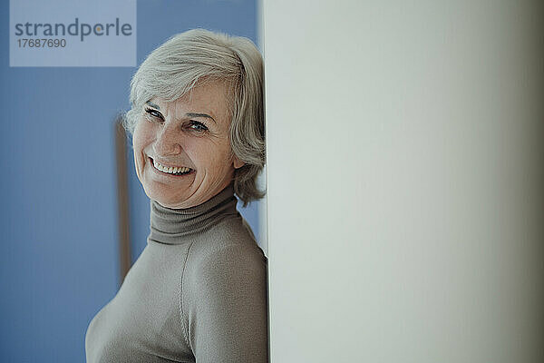 Cheerful senior woman with gray hair leaning on wall