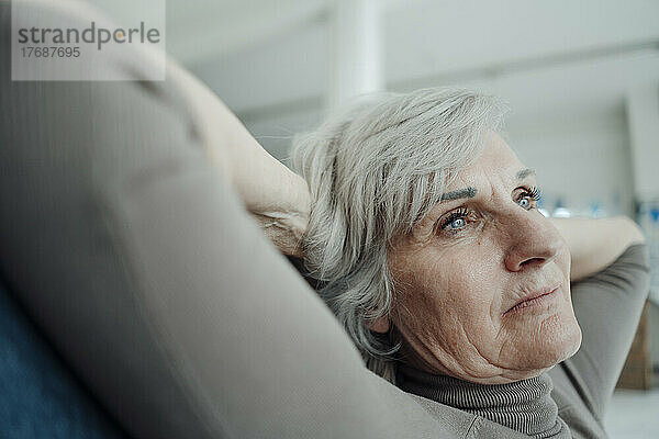 Ältere Frau sitzt mit den Händen hinter dem Kopf