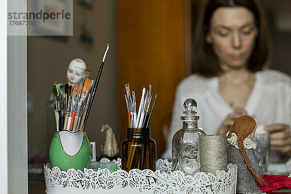 Puppenskulptur mit Pinseln und Kunsthandwerkerin im Hintergrund