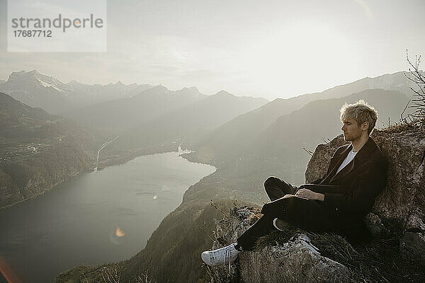 Junger Mann sitzt auf einem felsigen Berg
