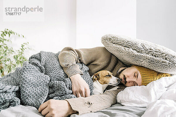 Erschöpfter Mann schläft voll bekleidet mit Hund im Bett