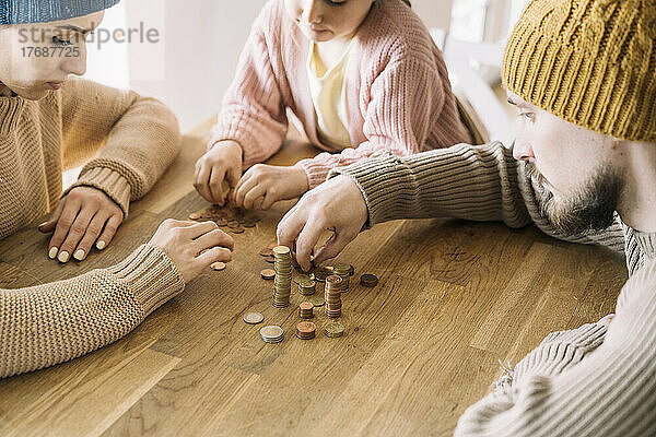 Arme Familie mit Wintermützen sitzt am Tisch und zählt Münzen