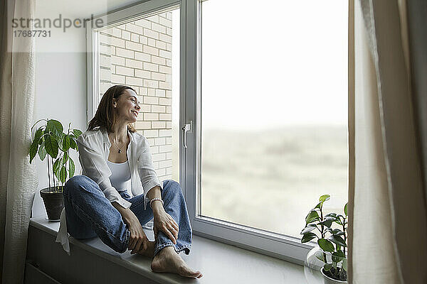 Glückliche reife Frau  die zu Hause auf der Fensterbank sitzt