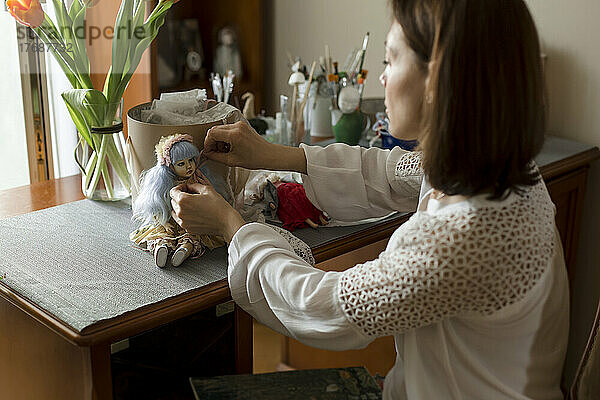 Frau dekoriert handgemachte Puppe auf Tisch zu Hause