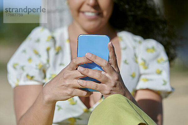 Junge Frau schreibt an einem sonnigen Tag SMS über ihr Smartphone