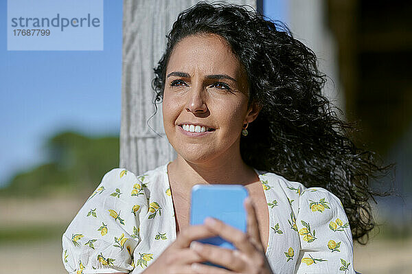 Nachdenklich lächelnde Frau mit Smartphone