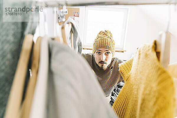 Junger Mann sucht im Kleiderschrank nach warmer Kleidung