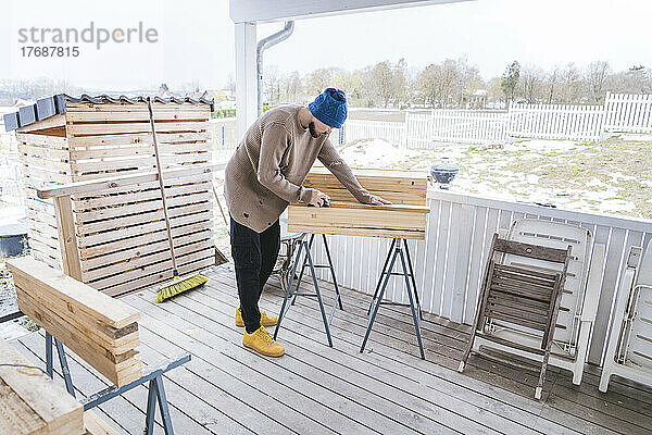 Junger Mann stapelt Holzbretter auf der Terrasse