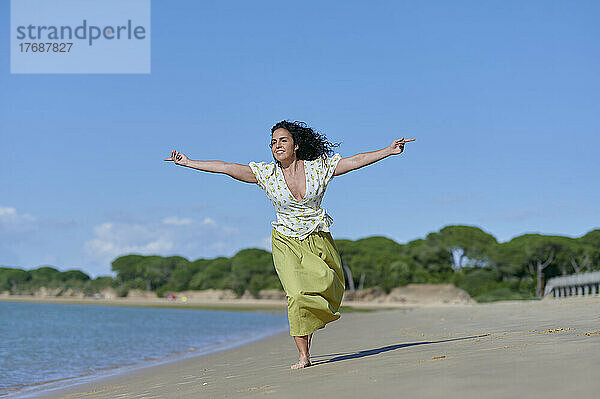 Glückliche Frau läuft an einem sonnigen Tag mit ausgestreckten Armen am Strand