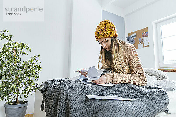 Woman with wooly hat sitting on bed checking bills